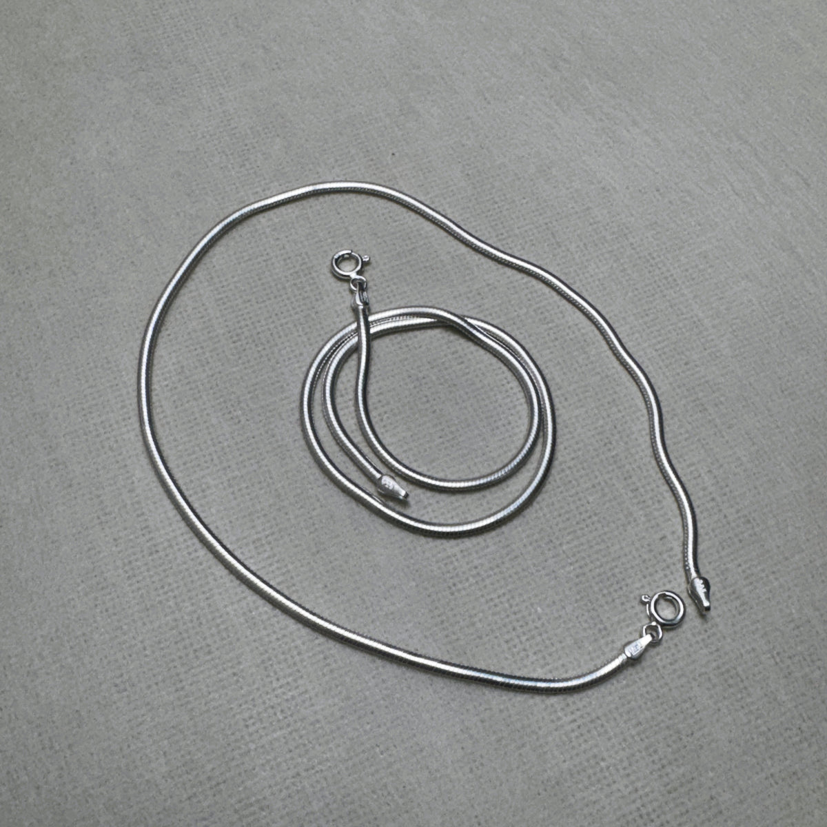 The pair of round snake chain silver anklets with both spring ring clasps showing.