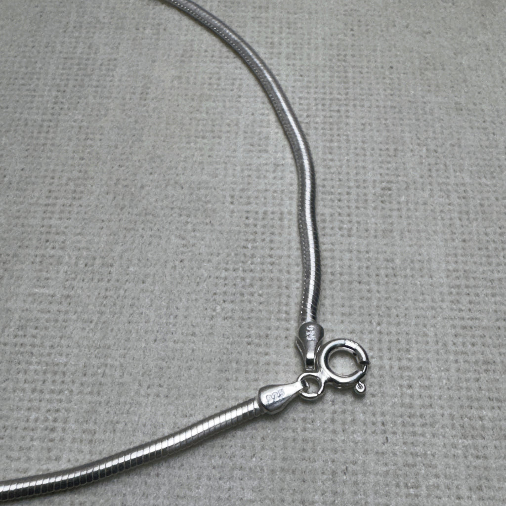 Close-up of the spring ring clasp and the 925 stamped tag on the snake chain anklet.