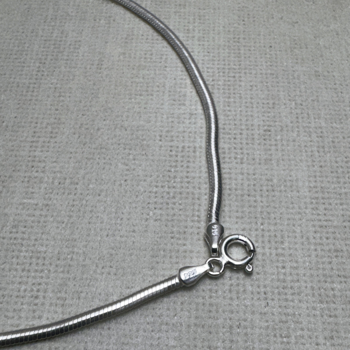 Close-up of the spring ring clasp and the 925 stamped tag on the snake chain anklet.