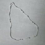 Sterling silver snake chain anklet with small polished bead stations, laid in a loop with its spring ring clasp.