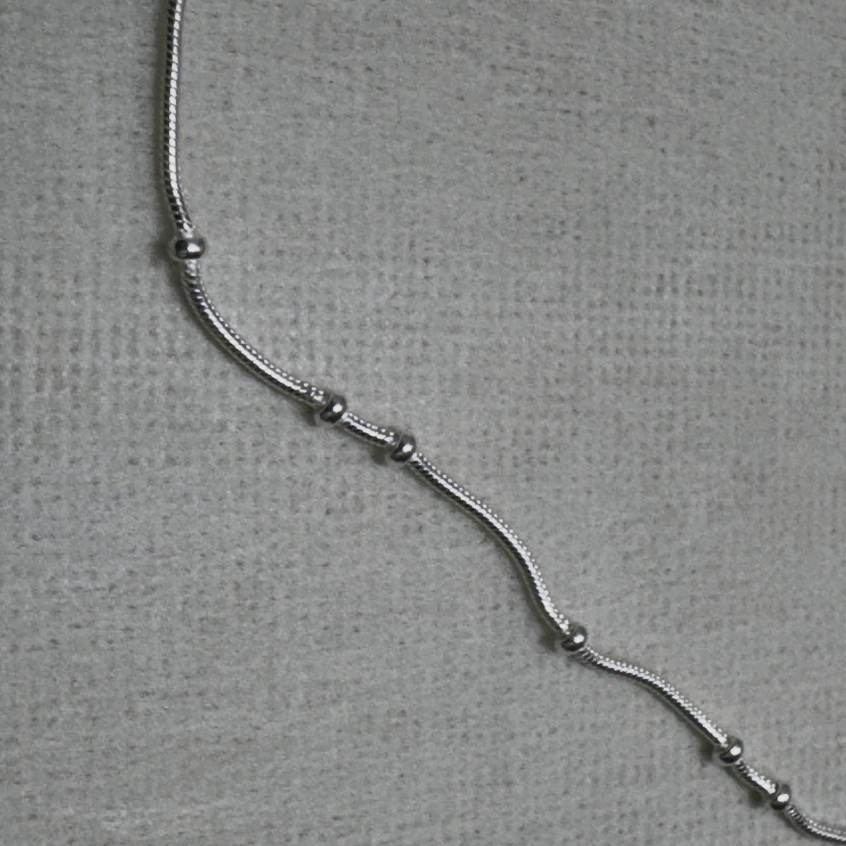 Close-up of the snake chain and the evenly spaced silver beads of the anklet.