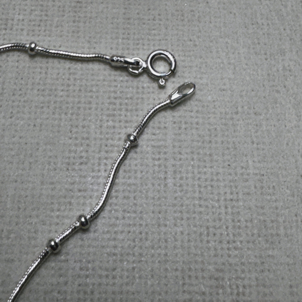 The spring ring clasp and end tag of the bead station silver anklet.
