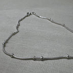The bead station snake chain anklet laid in a curve on a grey surface.
