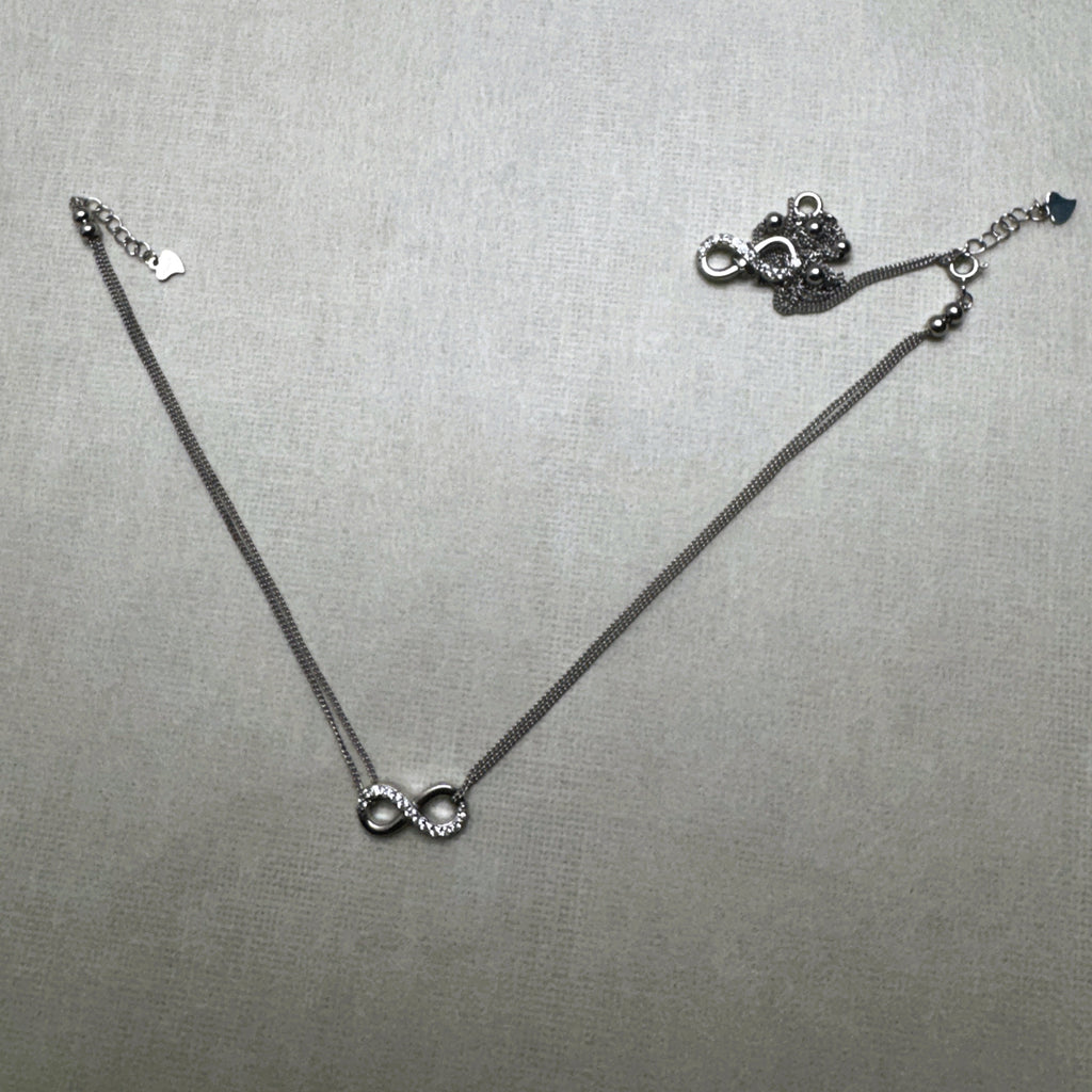 A pair of love knot silver anklets, one laid out and one gathered beside it.