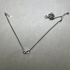 A pair of love knot silver anklets, one laid out and one gathered beside it.