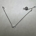 A pair of love knot American Diamond silver payal, one laid out and one gathered beside it.