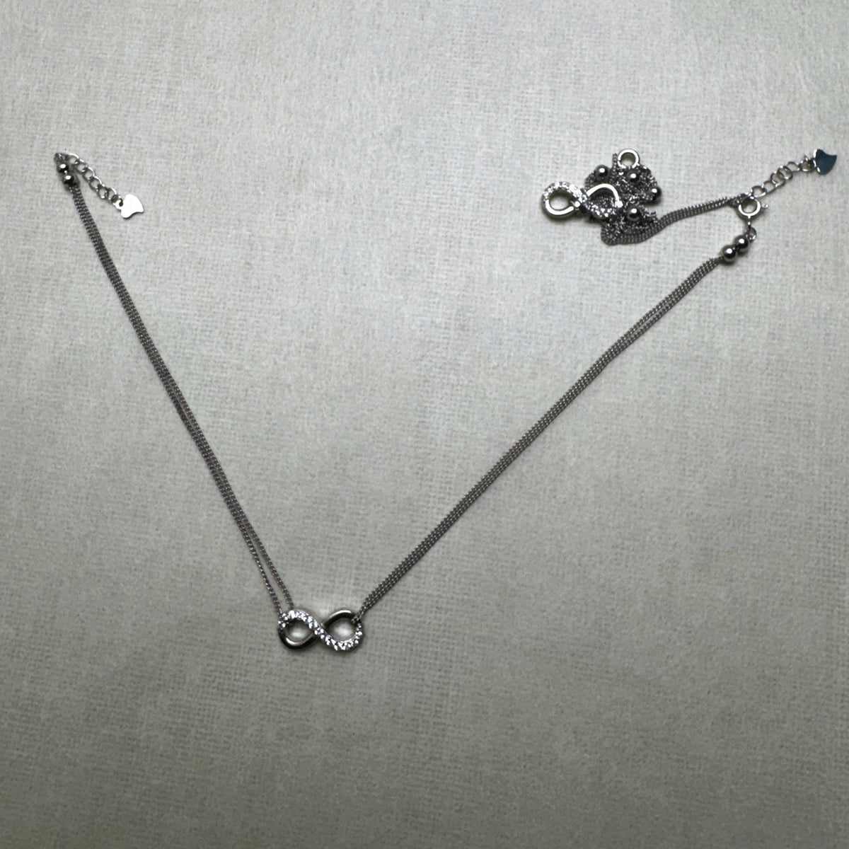 A pair of love knot American Diamond silver payal, one laid out and one gathered beside it.