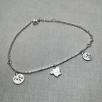 Sterling silver double rolo chain anklet with two emoji face charms and a cat charm, laid in a loop.
