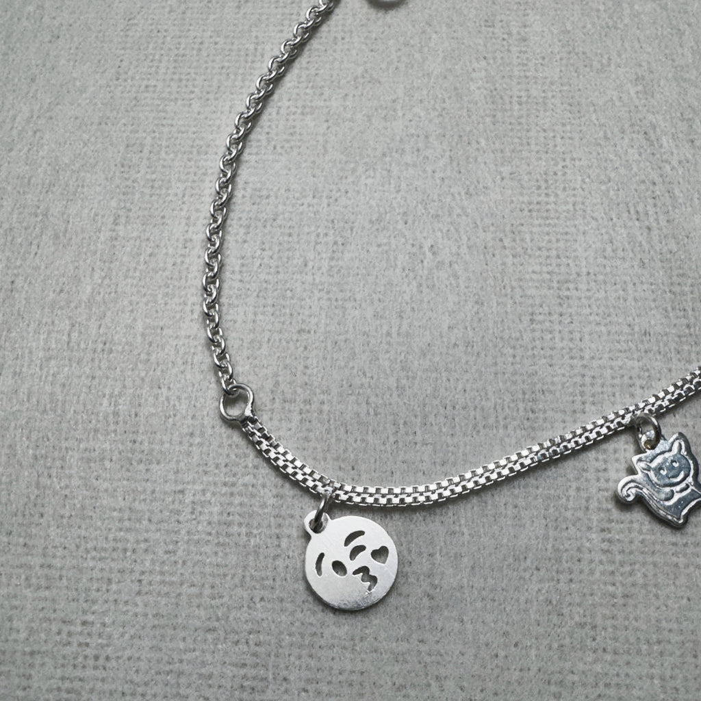 Close-up of the kissing emoji face charm and the cat charm on the silver anklet.