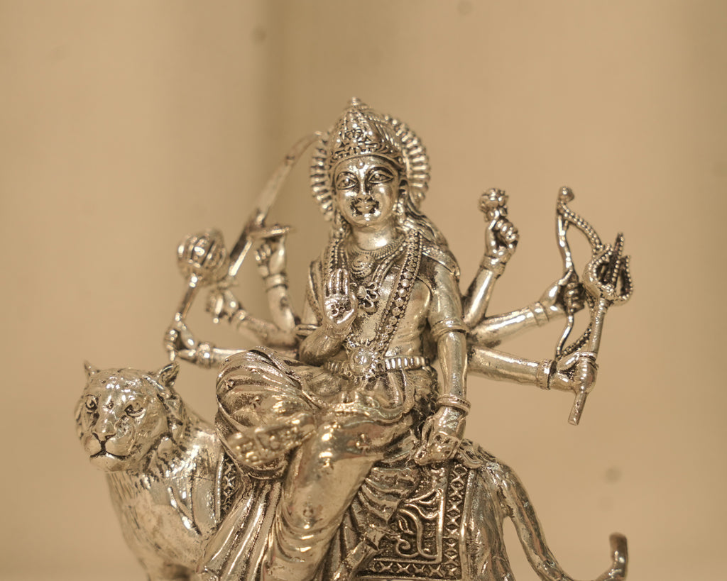 Close view of the silver Durga figure, her crown, her jewellery and the weapons in her eight hands.