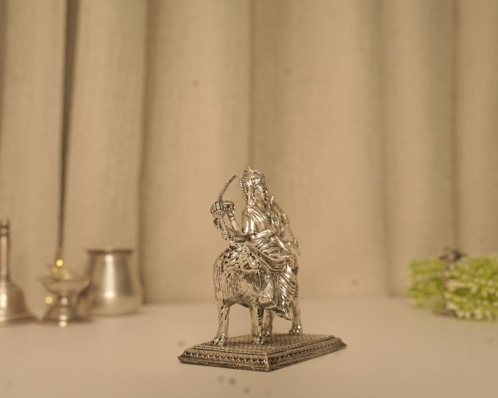 The silver Durga idol seen straight on from the front on a plain surface.