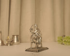 The silver Durga idol seen straight on from the front on a plain surface.