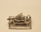 The silver Durga idol laid on its side, showing the pierced work along the edge of the base.