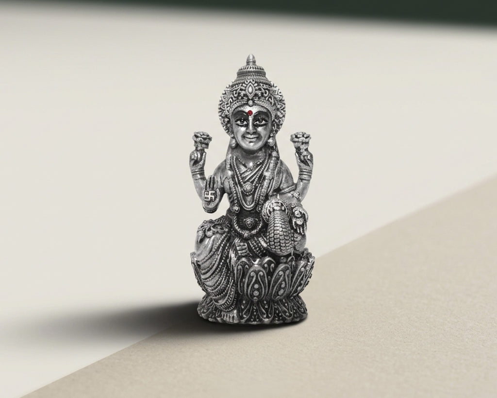Antique finish sterling silver Lakshmi idol seated on a lotus base, lit against a pale background.
