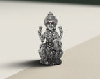 Antique finish sterling silver Lakshmi idol seated on a lotus base, lit against a pale background.
