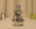 Large sterling silver Lakshmi idol on a broad lotus base, on a pale table with a silver pot behind.