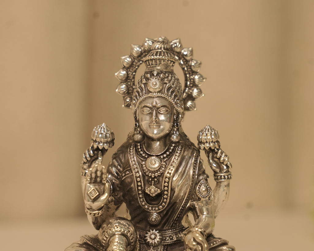 Close view of the silver Lakshmi figure, her crown, her necklaces and the lotus buds in her hands.