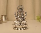 Large sterling silver Ganesh idol on a lotus base, on a pale table with a silver pot behind.