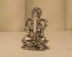 Antique finish sterling silver Ganesh idol with a tall crown, seated on a lotus base on a pale surface.