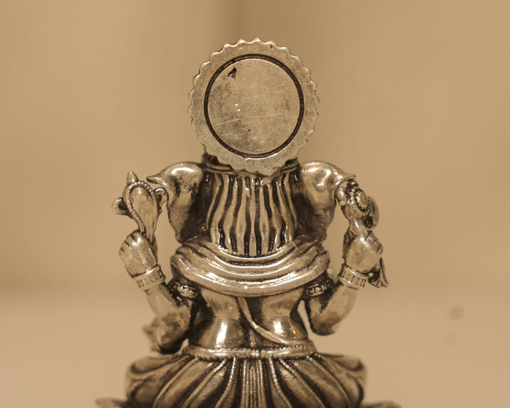 Close view of the back of the antique silver Ganesh idol and the round disc behind it.