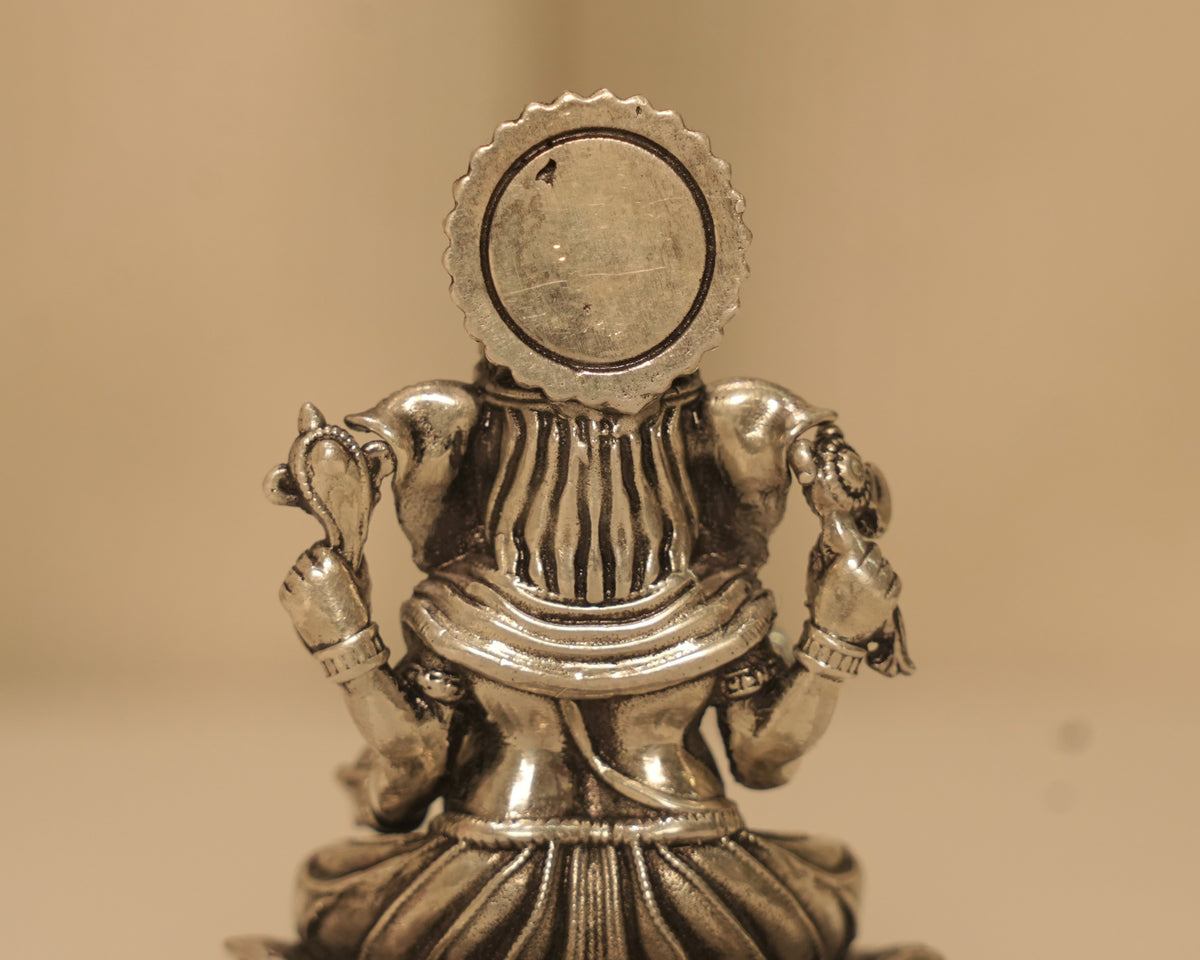 Close view of the back of the antique silver Ganesh idol and the round disc behind it.