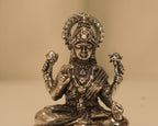 Close view of the silver Lakshmi figure, her crown, her necklaces and the lotus buds in her hands.