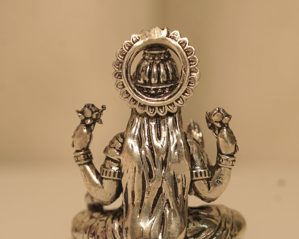 Close view of the back of the silver Lakshmi idol, showing the kalash set within the arch.