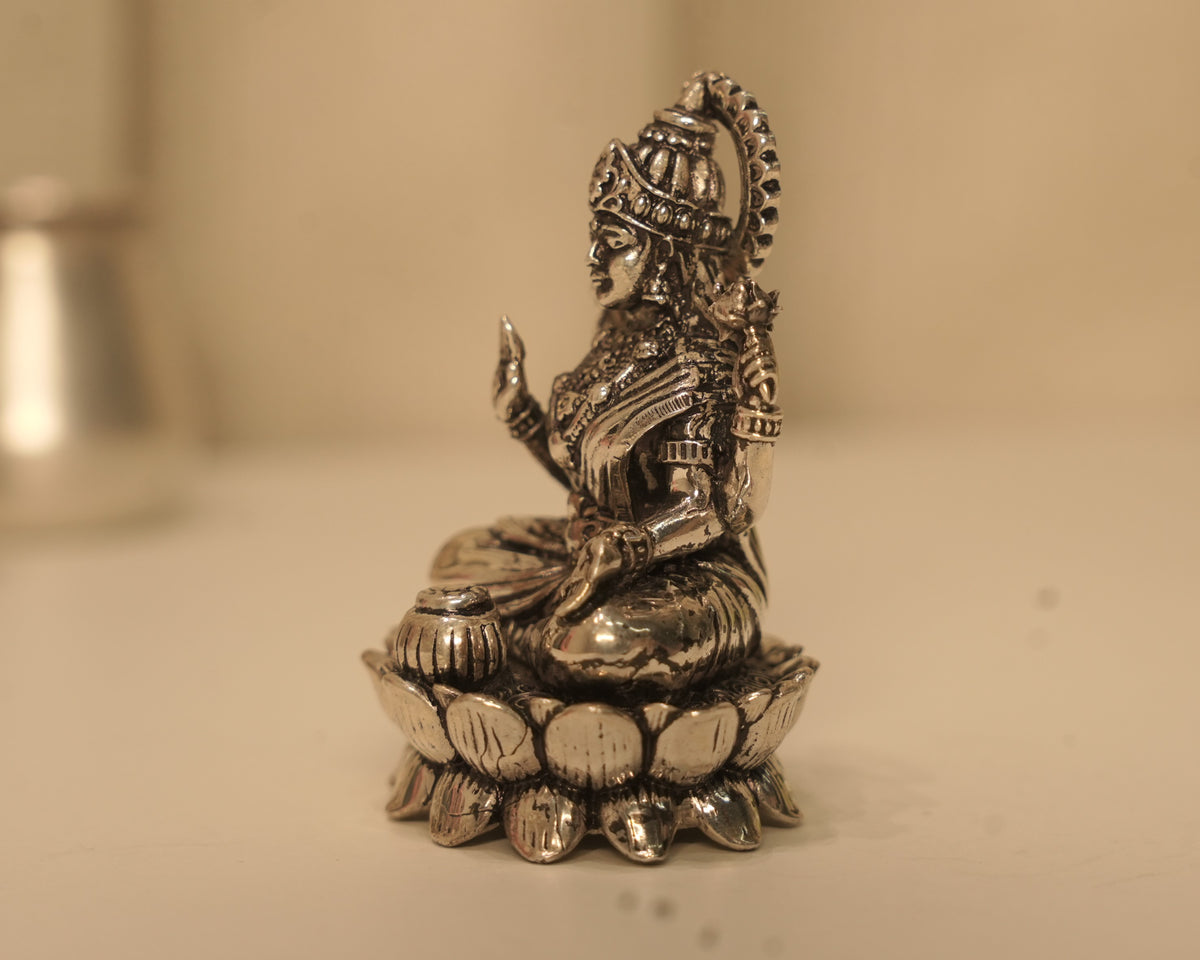 Side view of the silver Lakshmi idol, showing the crown and the lotus base in profile.