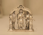 Close view of the three antique silver figures standing within the carved arch.