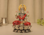 The enamelled silver Lakshmi idol seen straight on, with a silver pot and lamp behind.