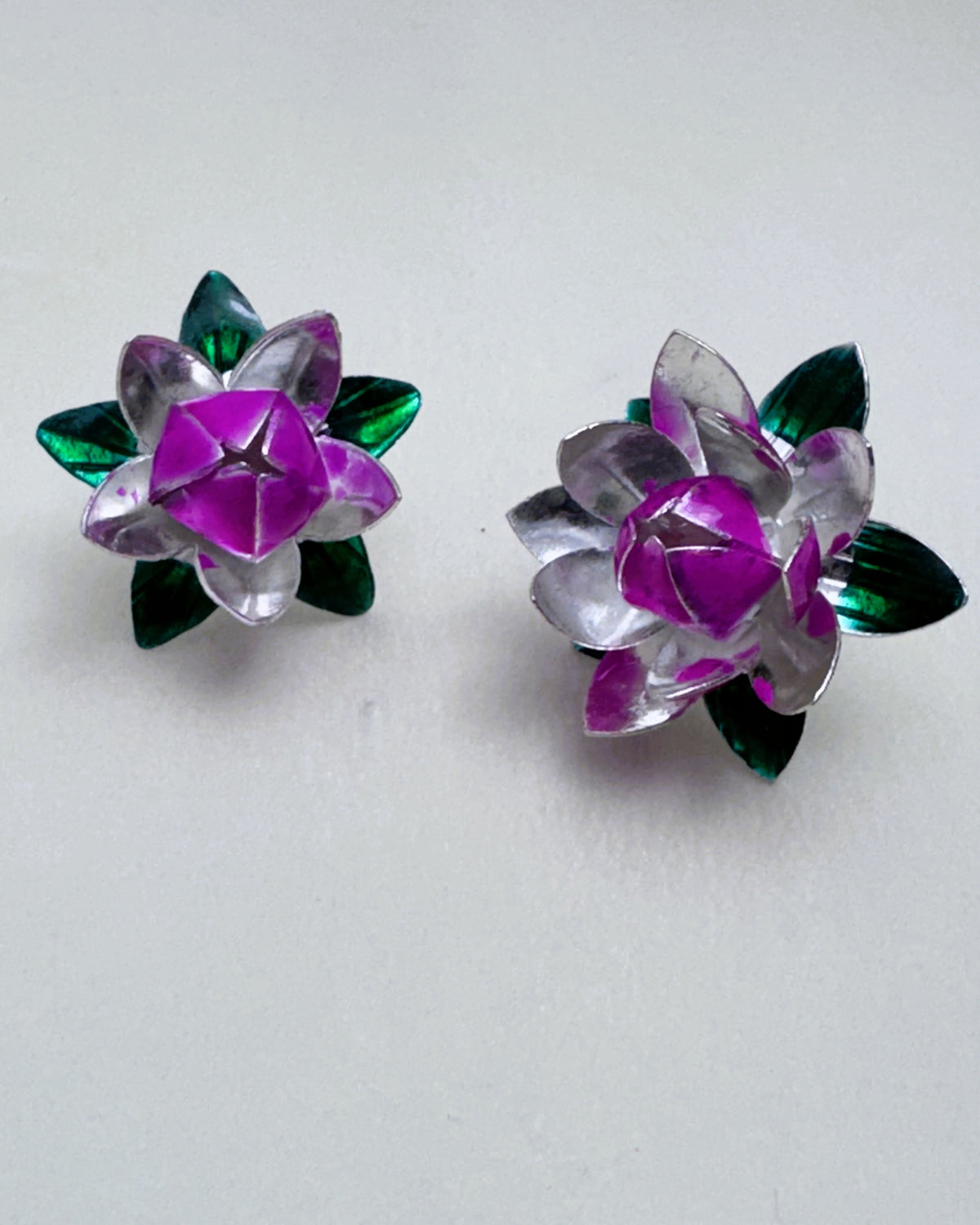 The large and small silver and pink enamel lotus flowers side by side on a white surface.