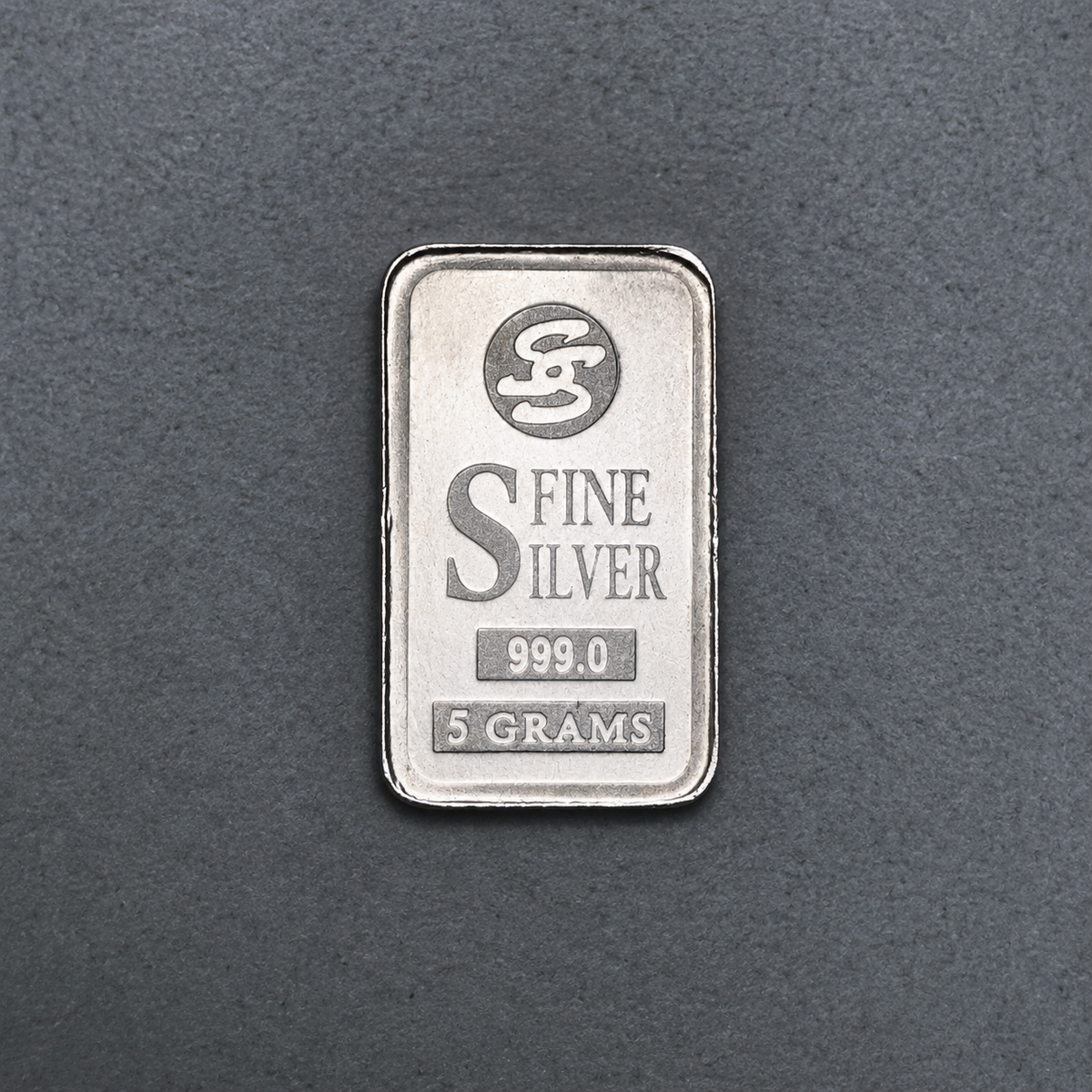 5 gram fine silver bar, front face stamped Fine Silver 999.0 and 5 grams, on a dark grey surface.
