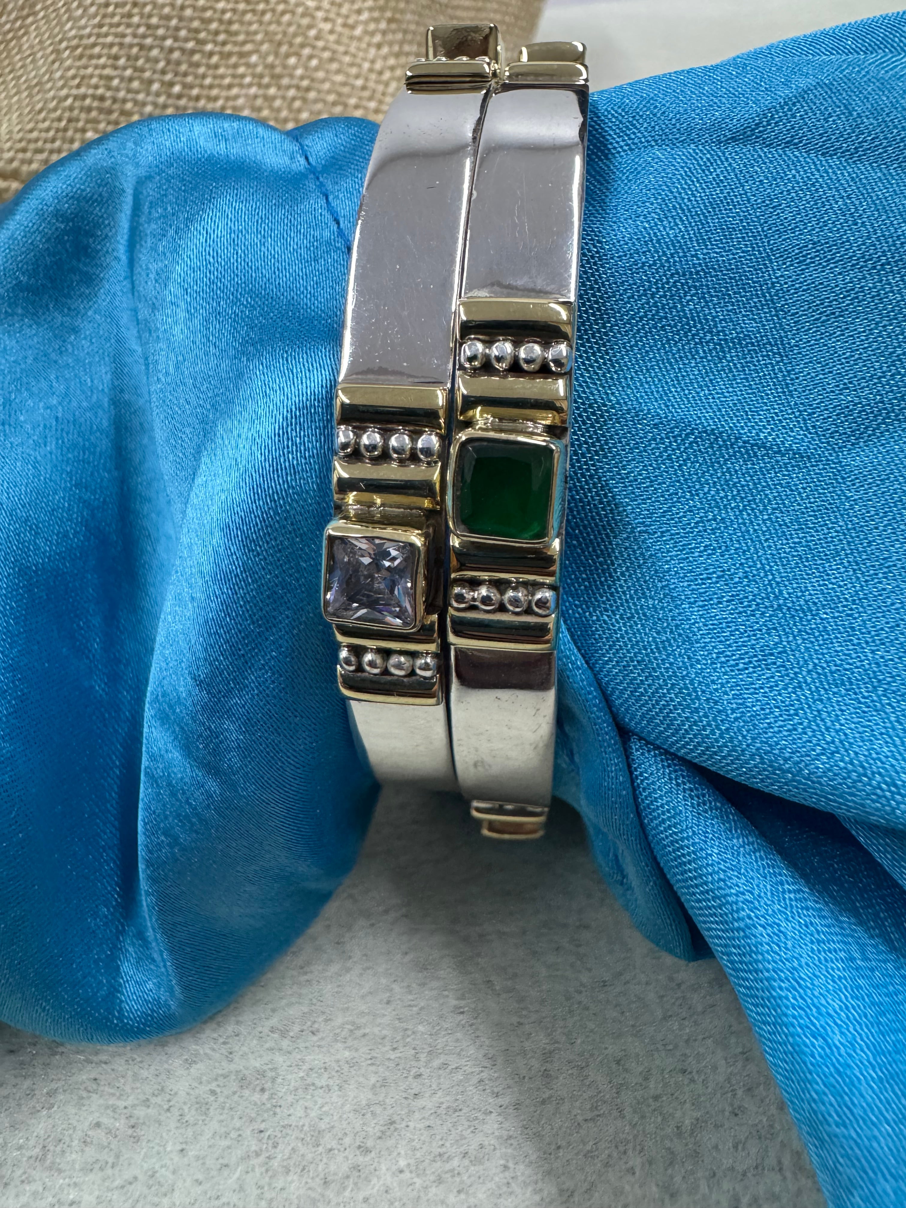Sterling silver bangles on blue silk, showing a green square stone and a colourless square stone in gold-tone bezel settings.