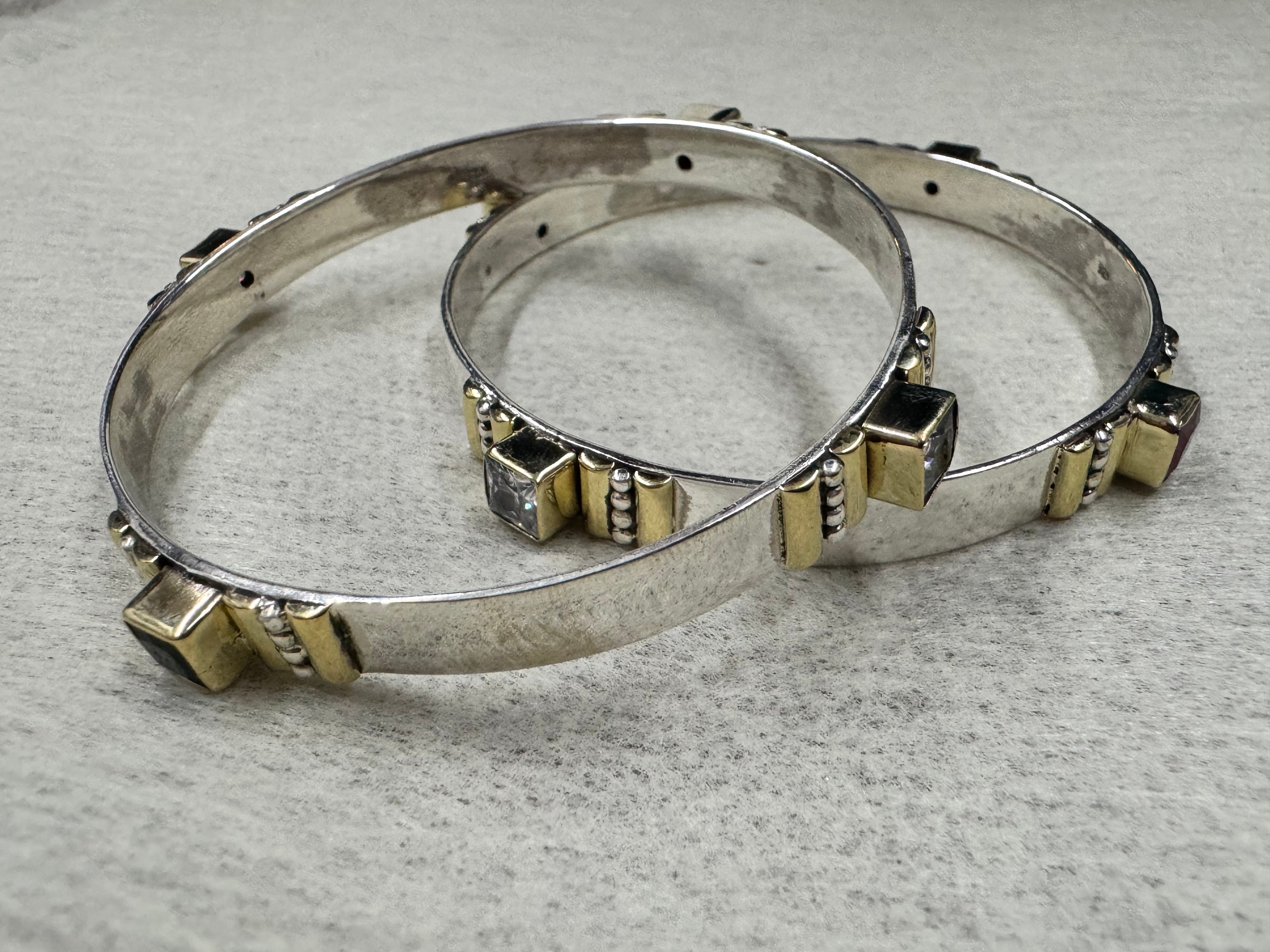 Sterling silver bangles on a grey surface, showing the plain inner face of the band and the raised gold-tone stone stations.