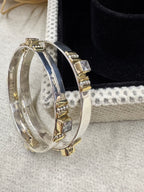 Sterling silver bangles beside a black jewellery box, with colourless square stones in gold-tone bezels and the tongue closure visible.