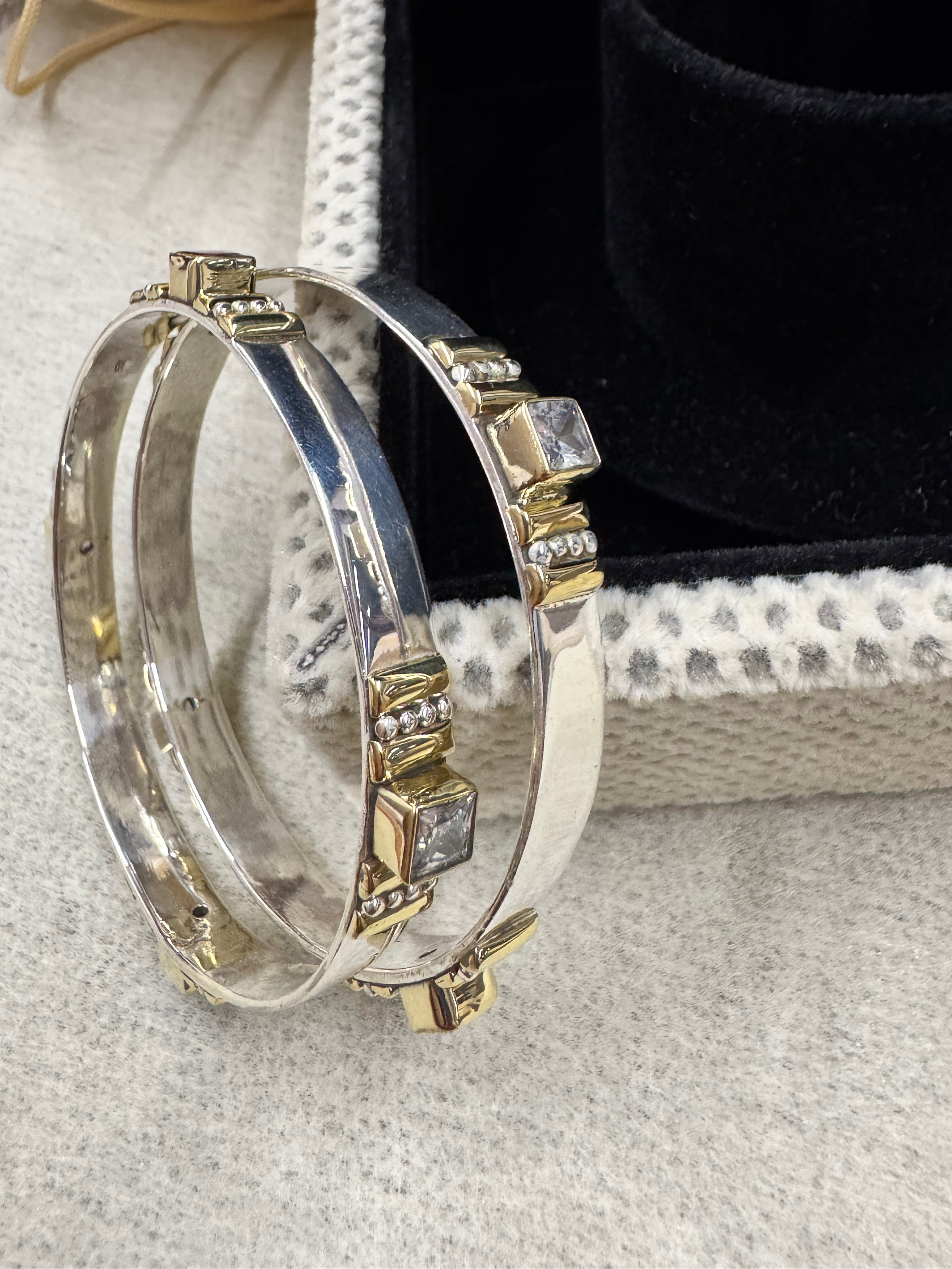 Sterling silver bangles beside a black jewellery box, with colourless square stones in gold-tone bezels and the tongue closure visible.