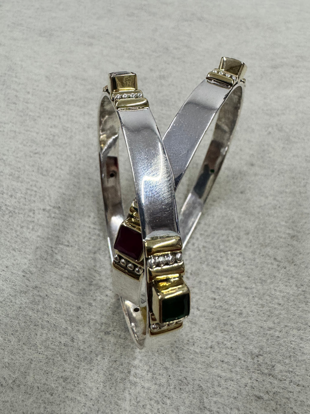 Overlapping sterling silver bangles on grey, showing the green and red stone stations and the point at which the band parts.