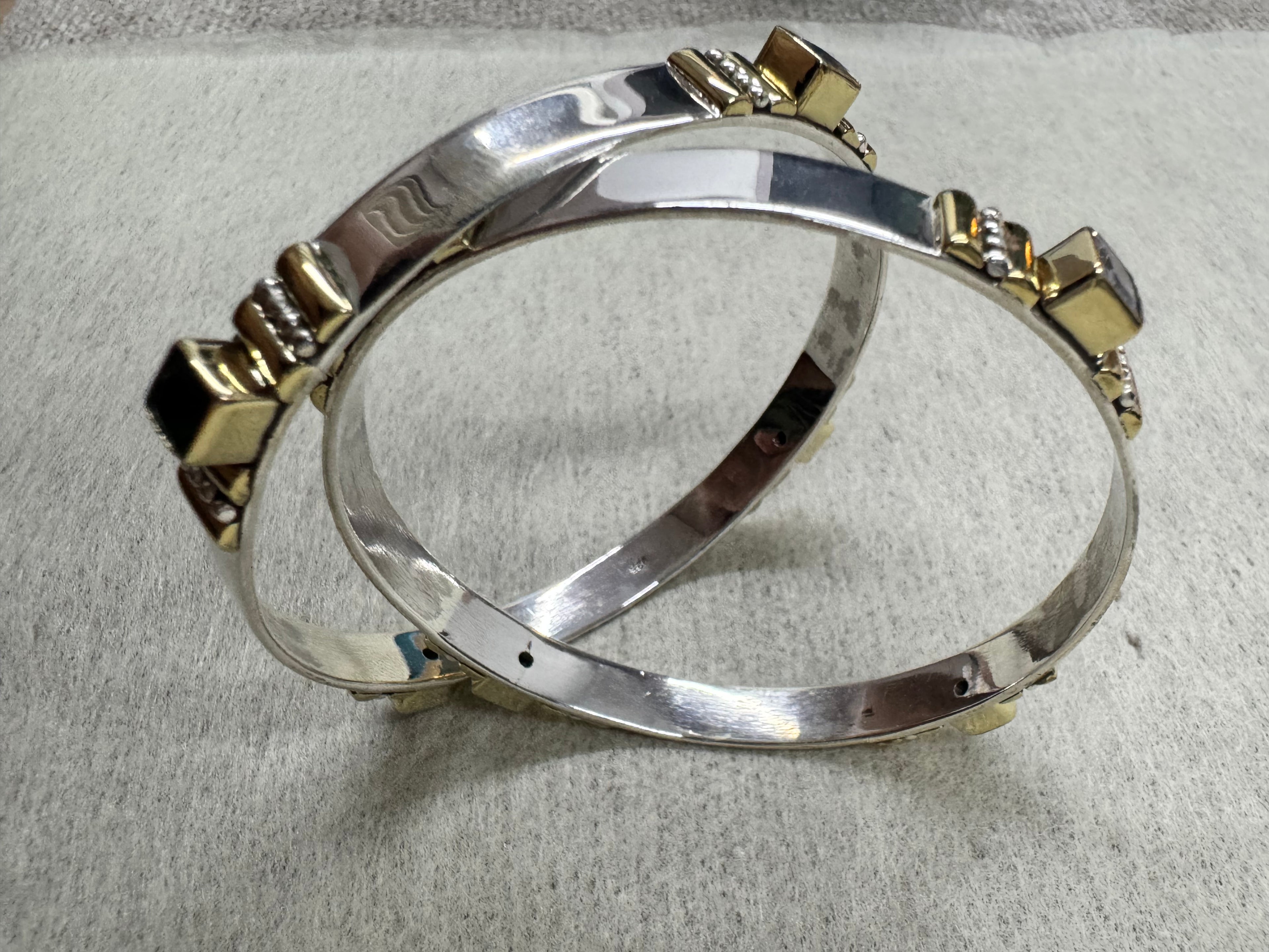 Sterling silver bangles seen from above, showing the plain polished band running between the gold-tone stone stations.