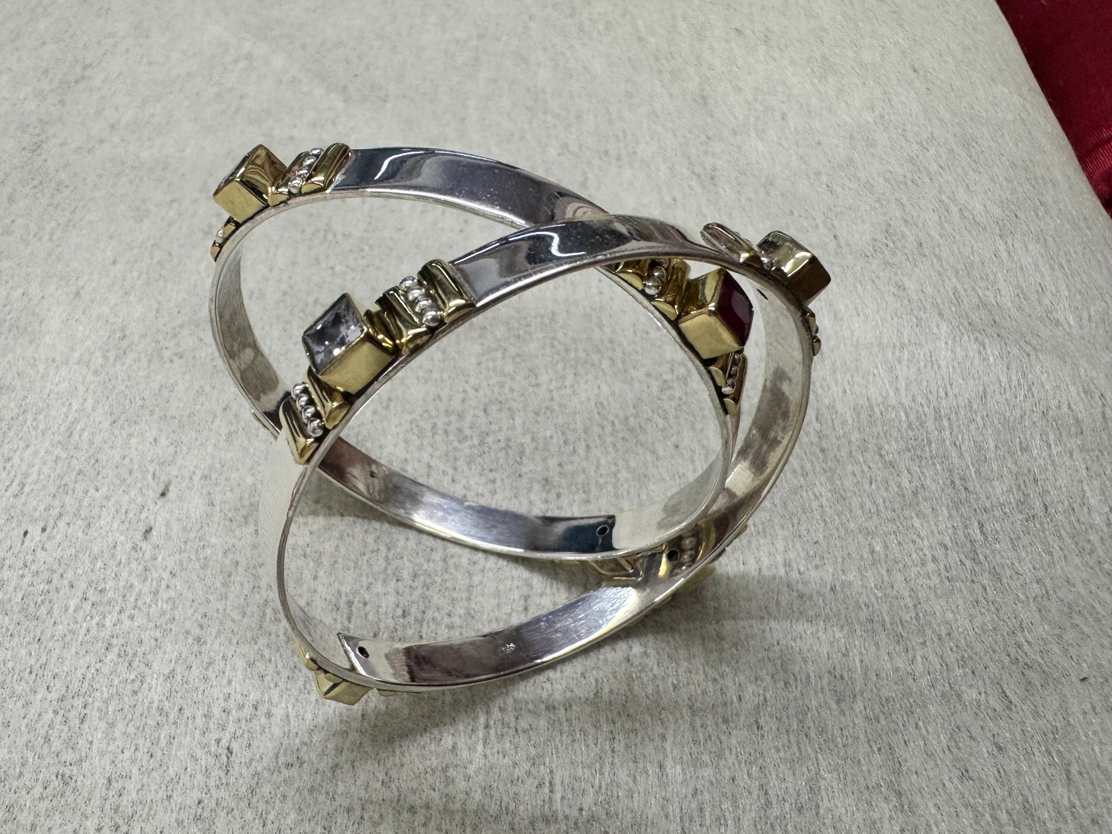 Angled view of the sterling silver bangles, showing the flat band profile and a colourless square stone in its gold-tone bezel.