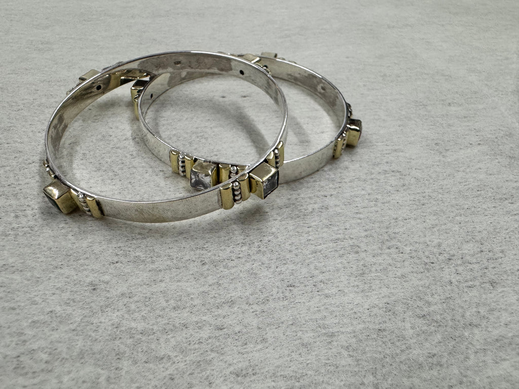 Sterling silver bangles laid flat on grey, with colourless and dark stones spaced around each band in gold-tone settings.