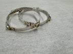 Sterling silver bangles laid flat on grey, with colourless and dark stones spaced around each band in gold-tone settings.