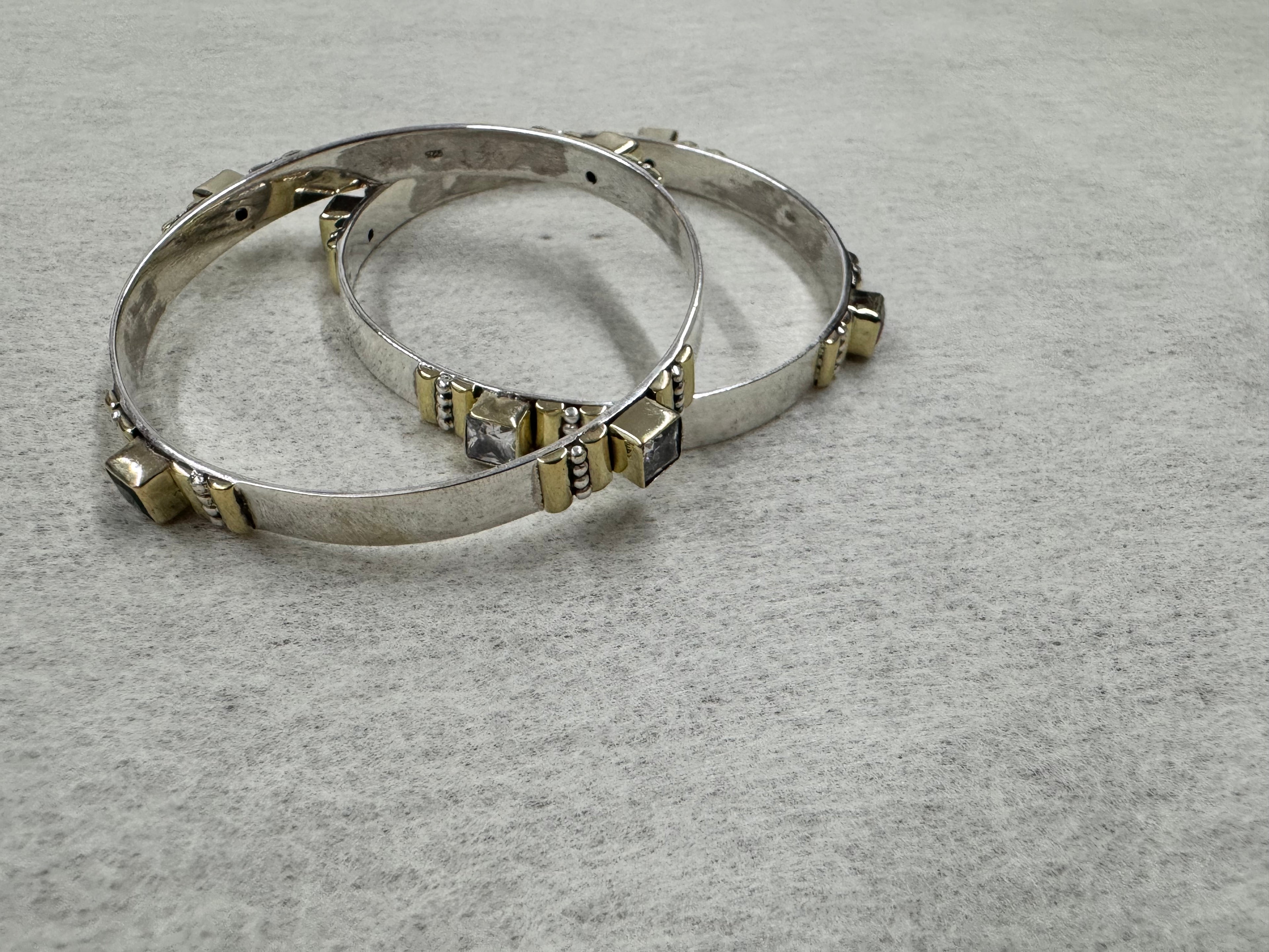 Sterling silver bangles laid flat on grey, with colourless and dark stones spaced around each band in gold-tone settings.
