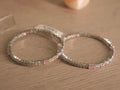 Pair of sterling silver bangles set with white American Diamond and soft pink rectangular stones, resting together on a shelf.