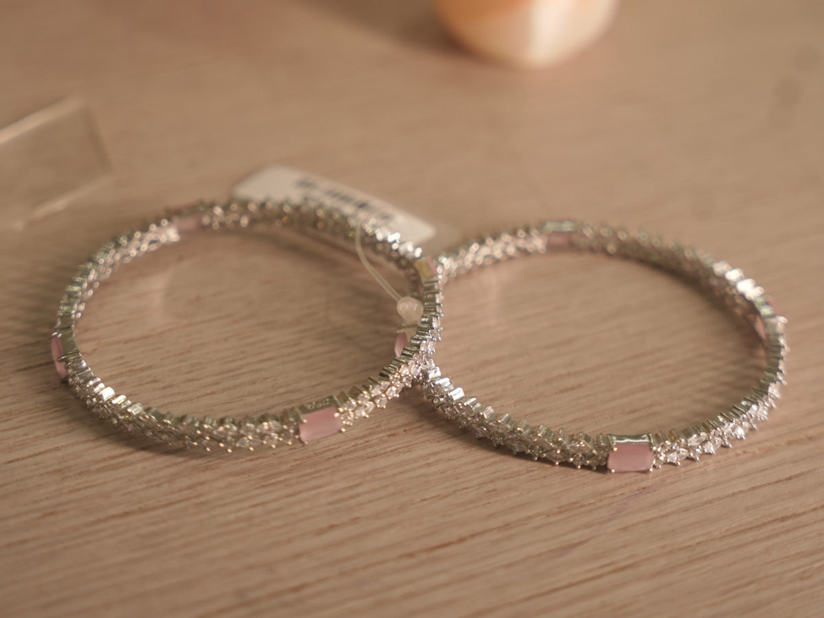 Pair of sterling silver bangles set with white American Diamond and soft pink rectangular stones, resting together on a shelf.