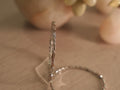 Slim sterling silver bangle standing upright, showing curving ribbon links with small hearts and squares set with American Diamond.