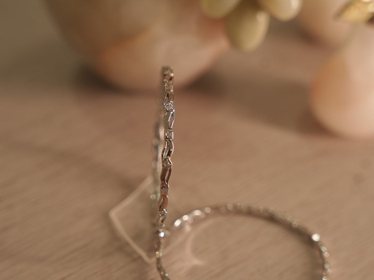Slim sterling silver bangle standing upright, showing curving ribbon links with small hearts and squares set with American Diamond.
