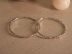 Pair of slim sterling silver bangles lying flat, showing the ribbon links and rose-tone touches around the band.