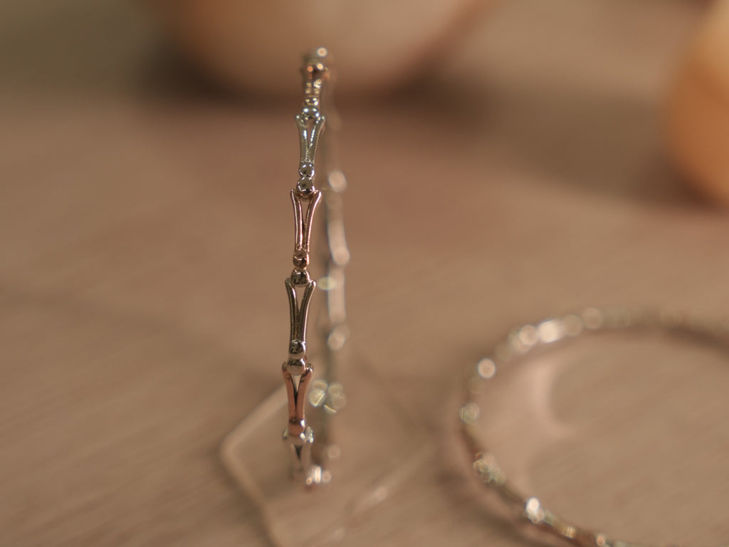 Slim two-tone sterling silver bangle standing upright, showing forked links meeting at polished bead nodes.