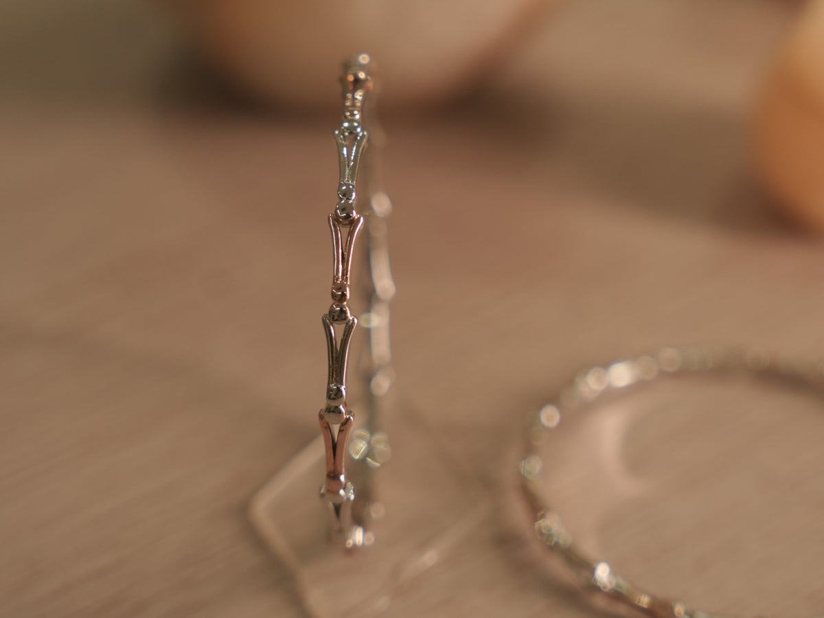 Slim two-tone sterling silver bangle standing upright, showing forked links meeting at polished bead nodes.
