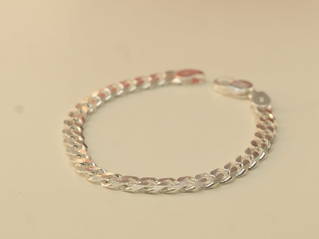 The silver curb chain bracelet laid in a circle, seen from a low angle.